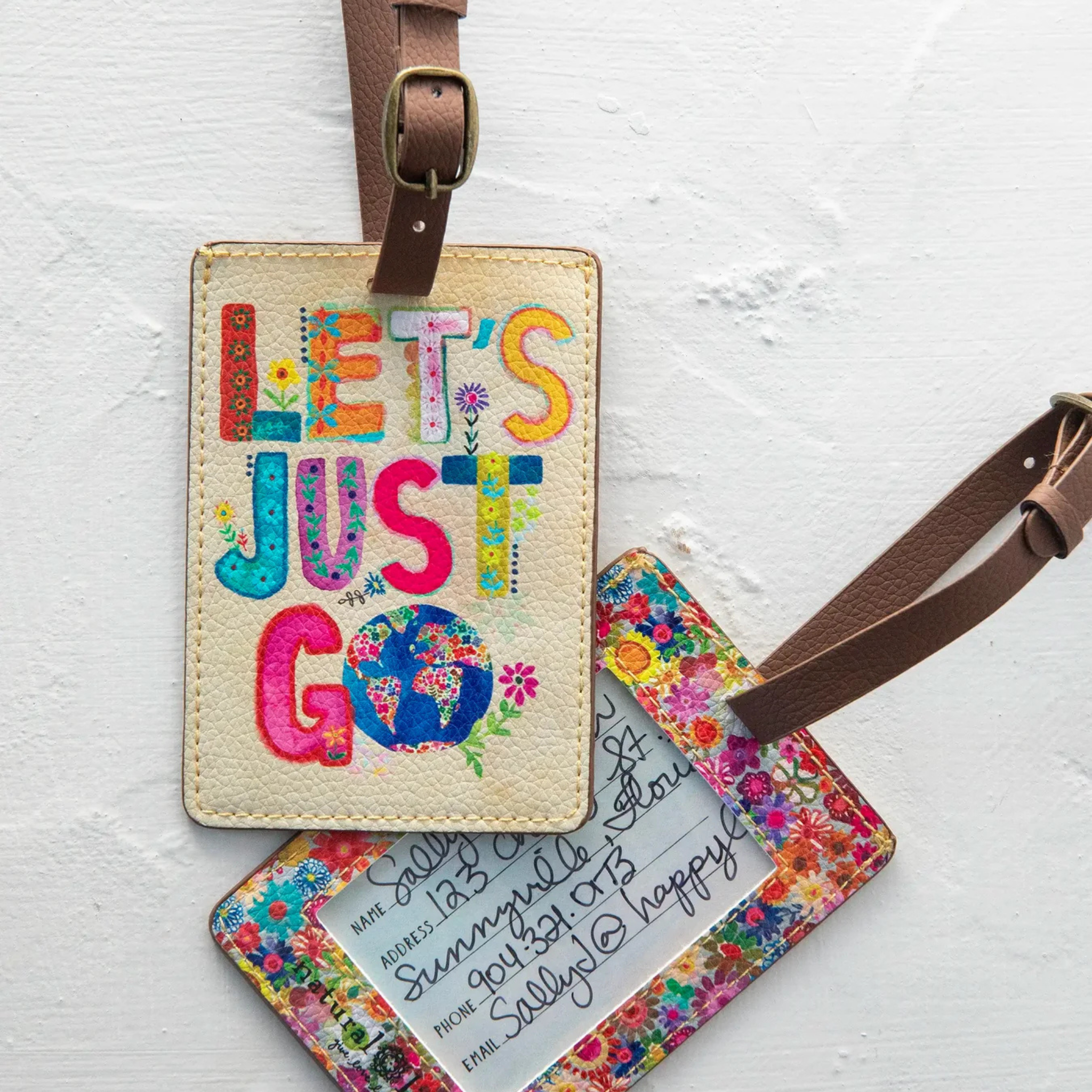 Natural Life Travel Happy luggage tag featuring "Let's Just Go" design, perfect for identifying your suitcase.
