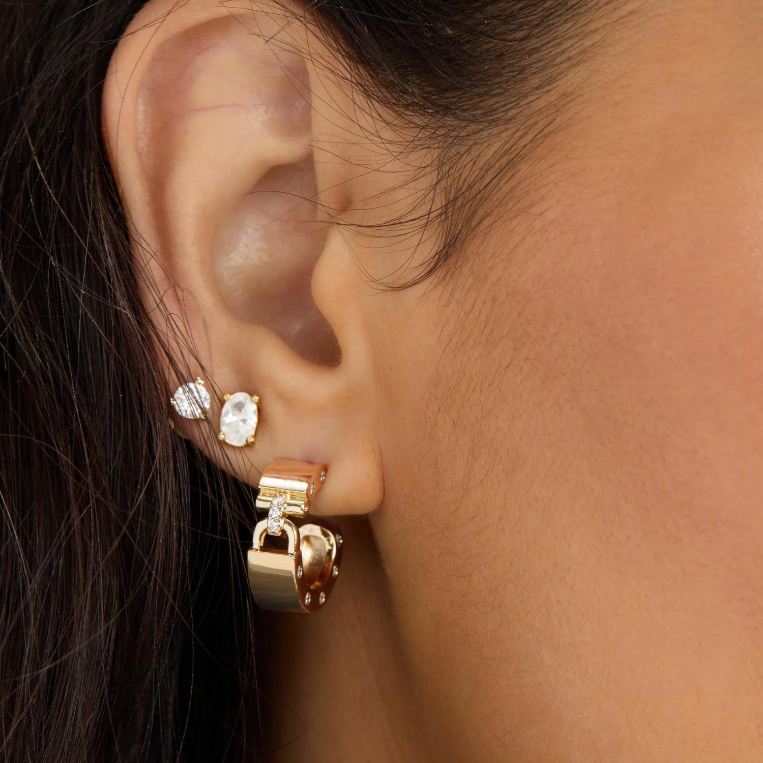Melinda Maria Ashley Lock Huggies earrings in gold with white diamondette details, showcasing a close-up of the sparkling jewelry.