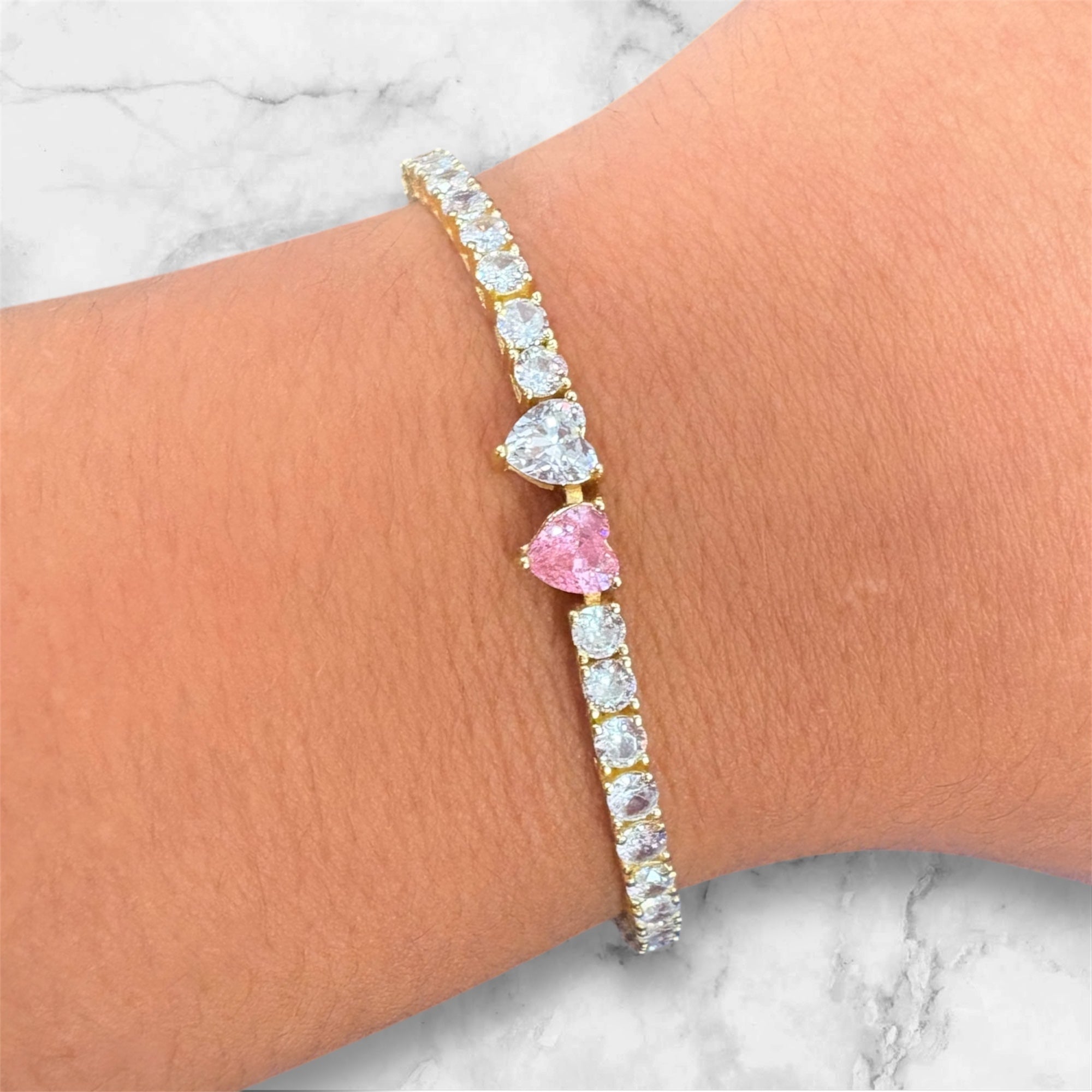 Bracelet with heart-shaped gemstones on a wrist against a marble background