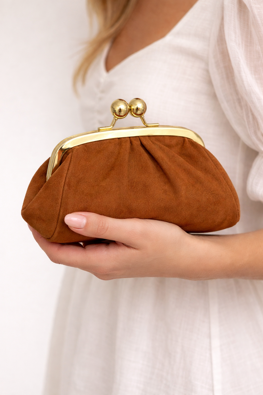 Brown clutch purse with gold clasp held by a person wearing a white dress.