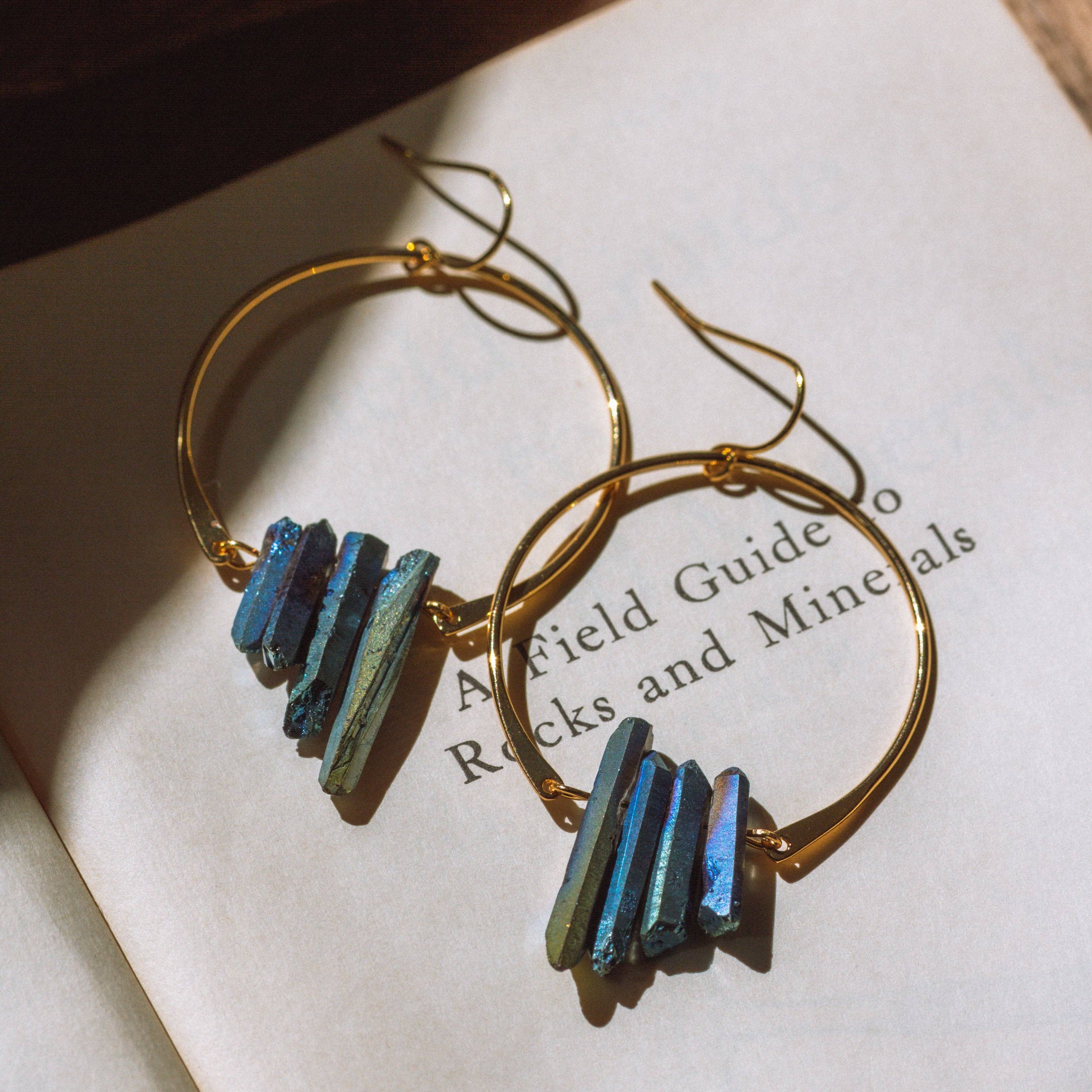 Gold hoop earrings with blue gemstones on an open book