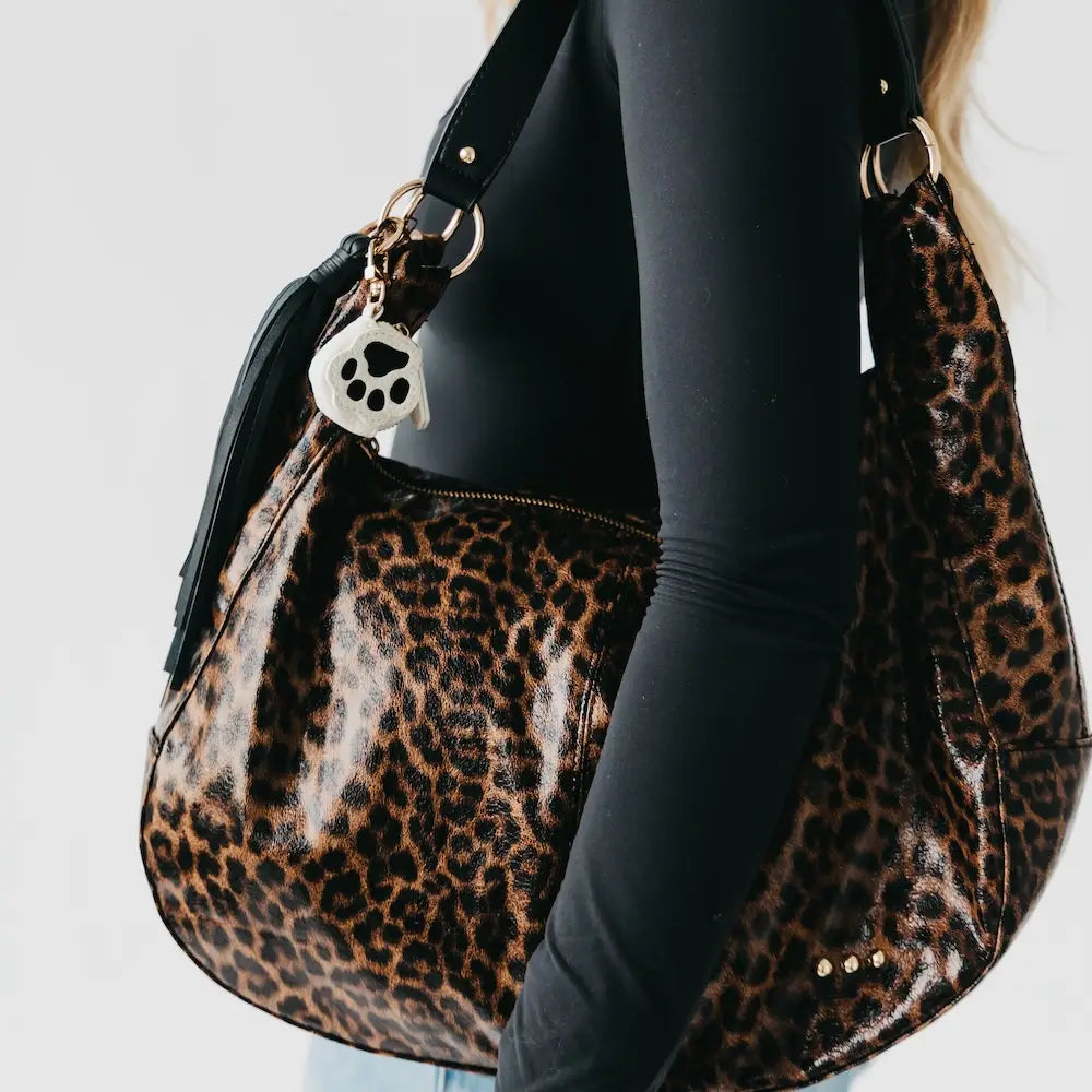 Leopard print handbag with a paw charm held by a person wearing a black outfit.