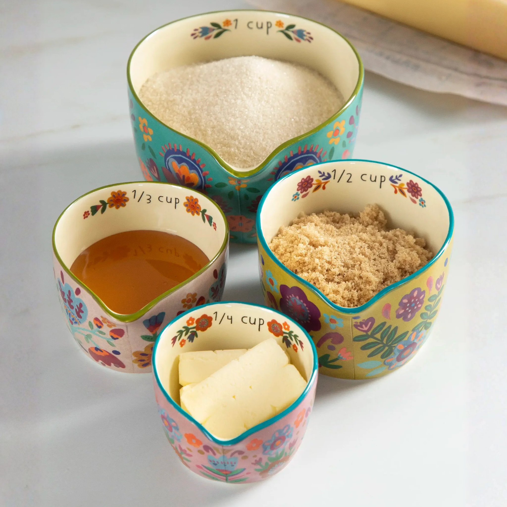 Ceramic nesting measuring cups with a folk flower design by Natural Life, showcasing vibrant colors and floral patterns.
