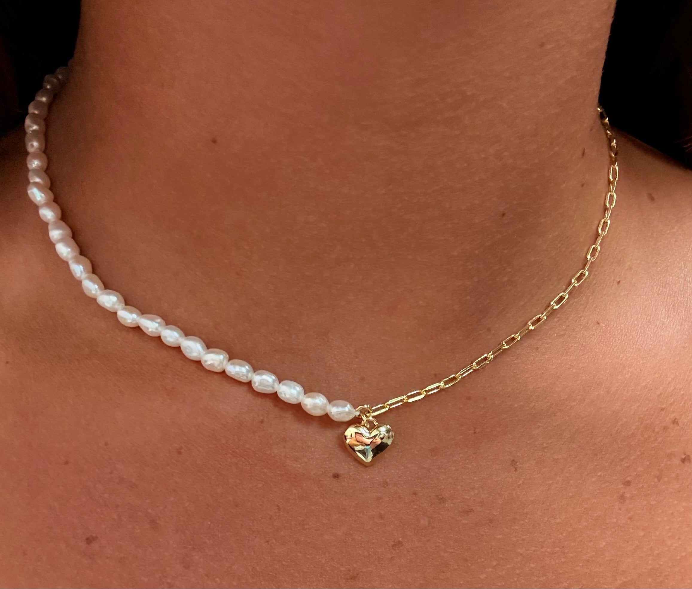 Pearl necklace with a gold chain and heart-shaped pendant on a person's neck.