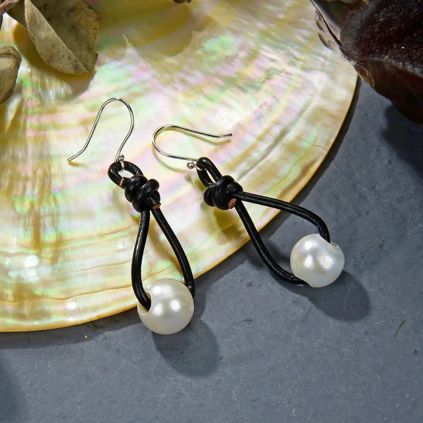Pearl earrings with black cord on a shell background