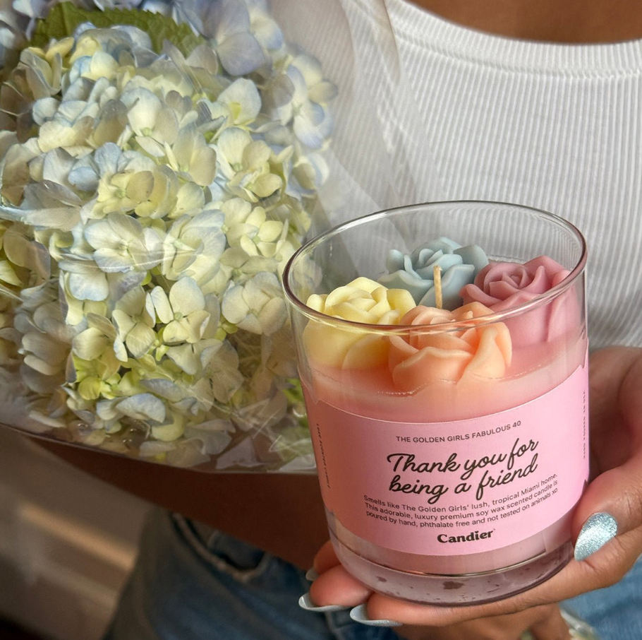 Candier Golden Girls flower candle with detailed floral design, featuring a decorative wax flower on top, in a clear glass holder.